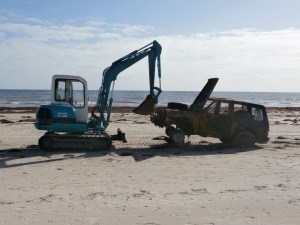 The front end loader dragging the recovery vehicle across the sand where a forklift's waiting to load it onto a tow truck