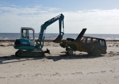 The front end loader dragging the recovery vehicle across the sand where a forklift's waiting to load it onto a tow truck
